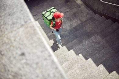 Photo of young delivery woman with thermal insulated bag for food walking up concrete steps